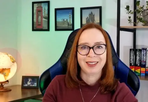 Teacher Rosana Sforca, criadora do curso Check-in no Inglês, sorrindo em seu escritório com elementos de viagem como globo terrestre e quadros de Londres ao fundo.